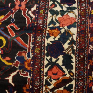 Close-up of a dark, multi-colored floral rug with a wide ivory border next to wood flooring.
