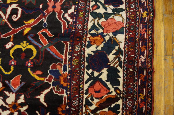 Close-up of a dark, multi-colored floral rug with a wide ivory border next to wood flooring.