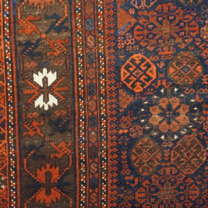 Close-up of a woven rug border and navy field with rust, brown, and white geometric motifs.