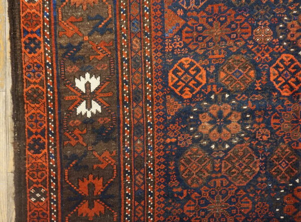 Close-up of a woven rug border and navy field with rust, brown, and white geometric motifs.