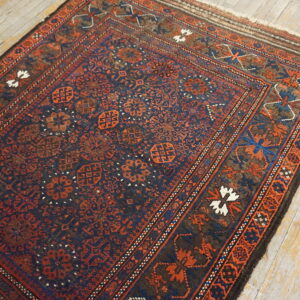 Dark blue and rust geometric rug with dense patterns rests on distressed light plank wood flooring.