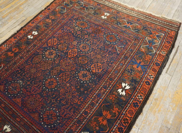 Dark blue and rust geometric rug with dense patterns rests on distressed light plank wood flooring.
