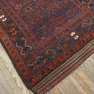 The corner of a dark blue, red, and brown patterned rug rests on distressed wooden floors.