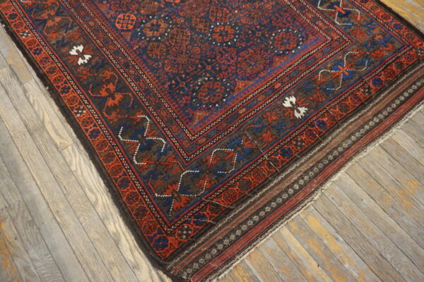 The corner of a dark blue, red, and brown patterned rug rests on distressed wooden floors.