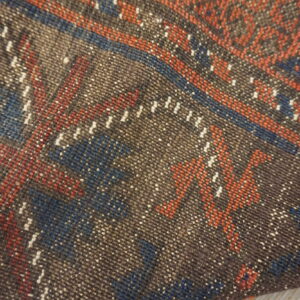 Tight weave texture of a rug showing speckled brown, rust, blue, and white geometric patterns.
