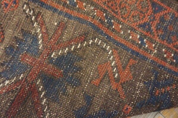 Tight weave texture of a rug showing speckled brown, rust, blue, and white geometric patterns.