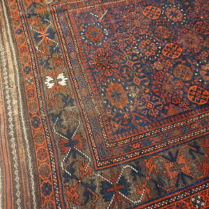 Low-pile tribal rug with dark blue and orange geometric patterns rests on distressed light wood floor.