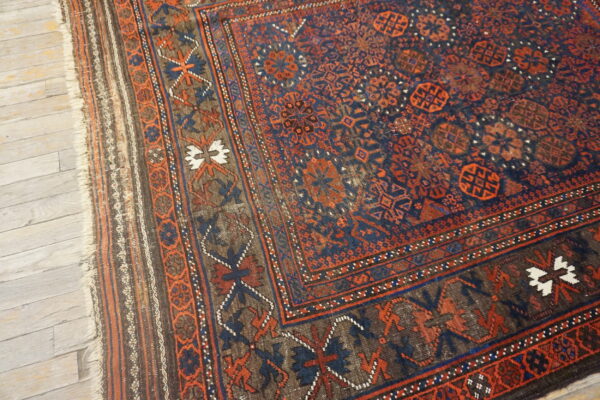 Low-pile tribal rug with dark blue and orange geometric patterns rests on distressed light wood floor.