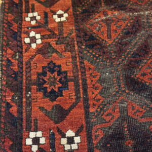 Textured, low-pile rug in red and navy geometric patterns resting on light plank flooring.