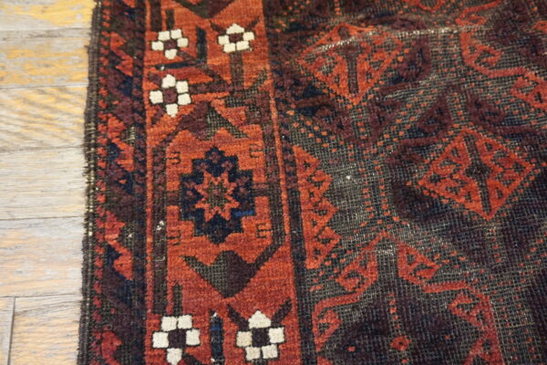 Textured, low-pile rug in red and navy geometric patterns resting on light plank flooring.