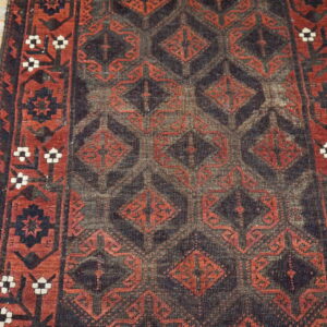 Distressed dark and red geometric runner rug with a low pile covers light hardwood flooring.