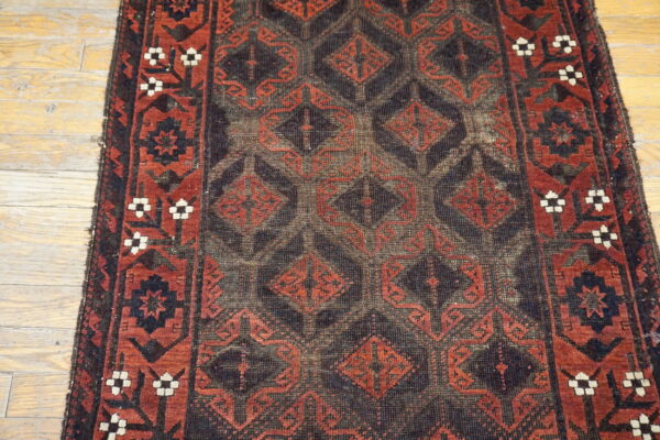 Distressed dark and red geometric runner rug with a low pile covers light hardwood flooring.