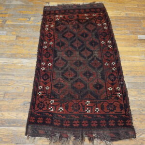 Worn, low-pile runner rug featuring deep red and black geometric patterns lies on distressed wooden flooring.
