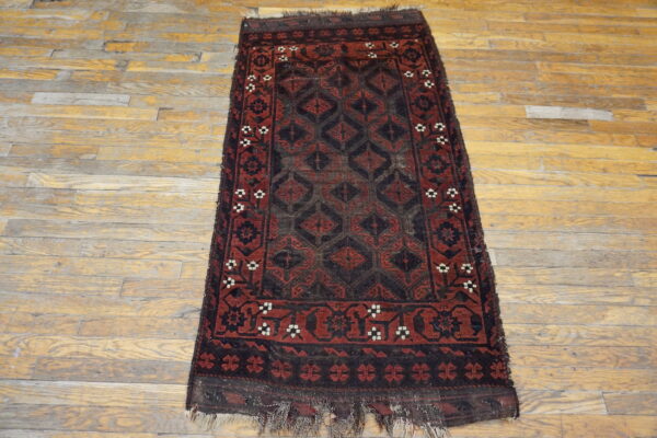 Worn, low-pile runner rug featuring deep red and black geometric patterns lies on distressed wooden flooring.