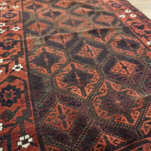 Deep red and dark brown geometric rug runner with a white floral border rests on light rustic wood planks.