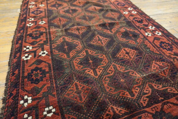 Deep red and dark brown geometric rug runner with a white floral border rests on light rustic wood planks.