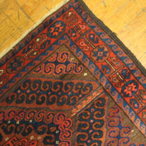 Close-up of a rug corner with geometric patterns in dark red, navy, and brown on rustic wood planks.