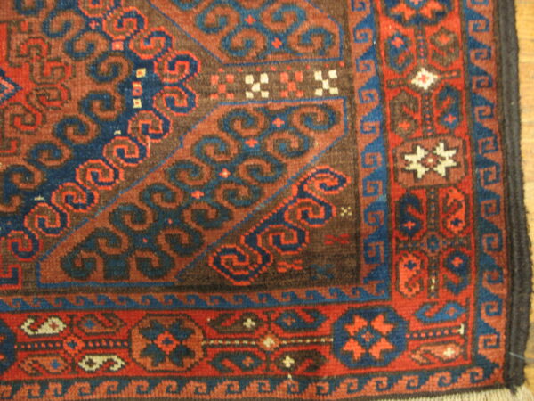 Close view of a rust and dark blue patterned rug border on light wooden floorboards.