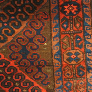 A close-up of a medium-pile rug with complex red, blue, and brown geometric patterns on wood flooring.