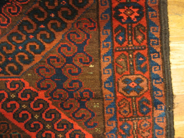 A close-up of a medium-pile rug with complex red, blue, and brown geometric patterns on wood flooring.