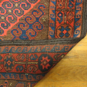 The corner of a red and blue patterned rug, showing the dense pile and woven reverse on wood floors.