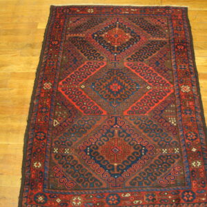 Low-pile geometric rug in red, dark blue, and brown with repeating medallion shapes on light wood planks.