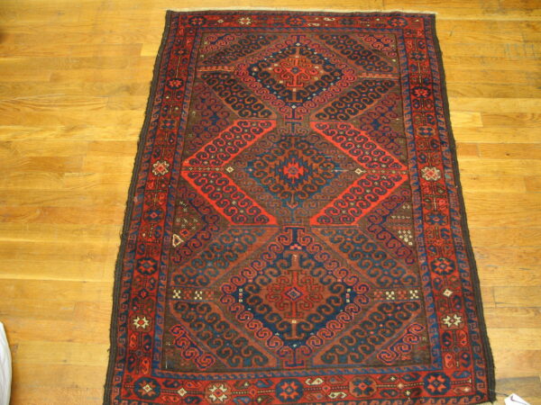 Low-pile geometric rug in red, dark blue, and brown with repeating medallion shapes on light wood planks.