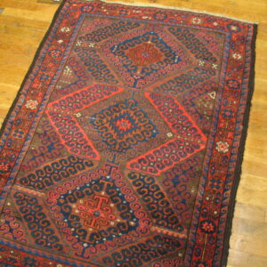 Geometric rug featuring red and blue tribal designs on a brown field over wood plank floors.