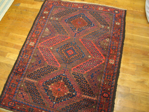 Geometric rug featuring red and blue tribal designs on a brown field over wood plank floors.