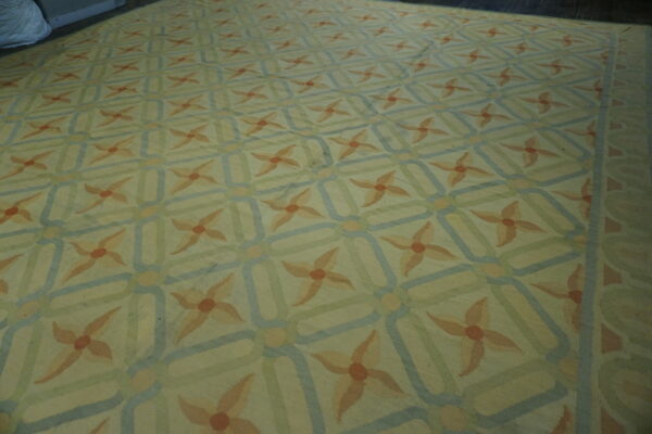 Low-pile rug featuring peach floral medallions connected by blue and green interlocking geometric lines.