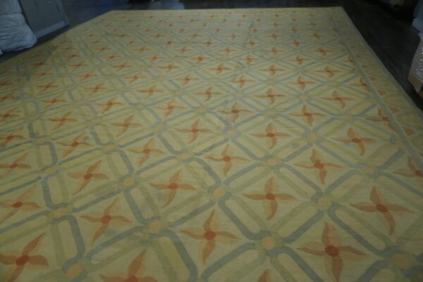 Low-pile rug with a pale yellow ground, blue geometric overlay, and repeating peach flower medallions.