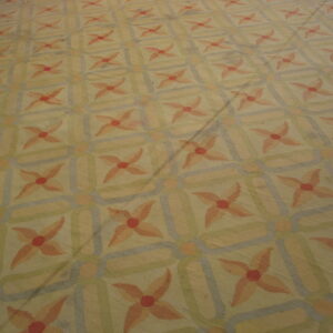 Muted, low-pile rug featuring peach floral motifs within an interlocking geometric pattern of yellow, green, and blue.
