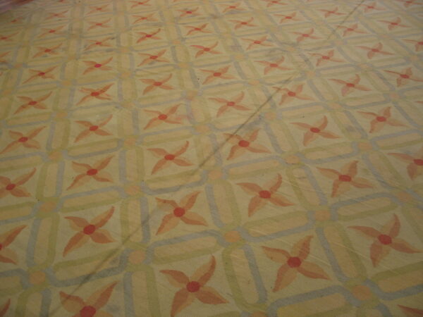 Muted, low-pile rug featuring peach floral motifs within an interlocking geometric pattern of yellow, green, and blue.