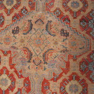 Detailed view of a low-pile rug showing intricate red, tan, and slate geometric patterning.