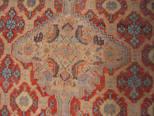 Detailed view of a low-pile rug showing intricate red, tan, and slate geometric patterning.