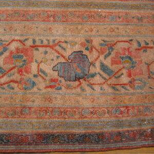 Detail of a rug showing medium pile and striped borders with muted blue, terracotta, and tan floral motifs.