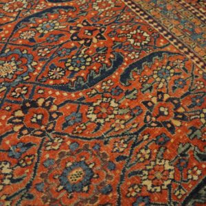 Intricate low-pile rug featuring a rust-orange background with dense navy, cream, and teal floral patterns.