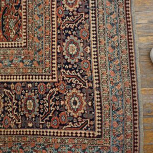Detailed view of a traditional rug corner in navy, terracotta, and light blue on distressed wood planks.