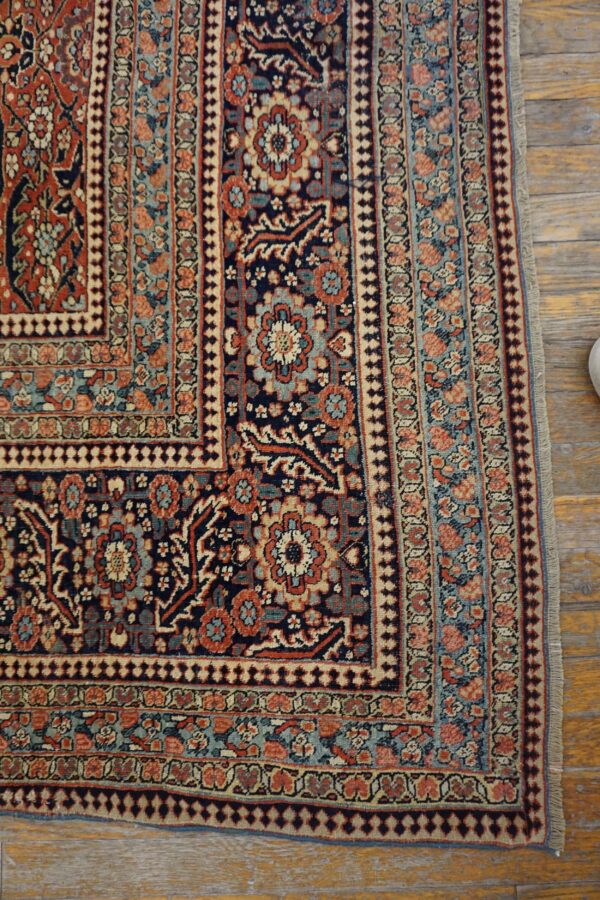 Detailed view of a traditional rug corner in navy, terracotta, and light blue on distressed wood planks.