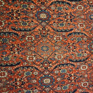 Detail of a low-pile rug featuring dense rust red, navy, and cream floral repeating patterns.