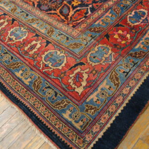 Traditional rug corner featuring detailed red, blue, and navy borders on worn hardwood flooring.