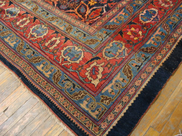 Traditional rug corner featuring detailed red, blue, and navy borders on worn hardwood flooring.
