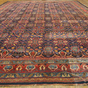 Ornate area rug with repeating red and blue floral patterns and thick, multicolored borders on wood flooring.