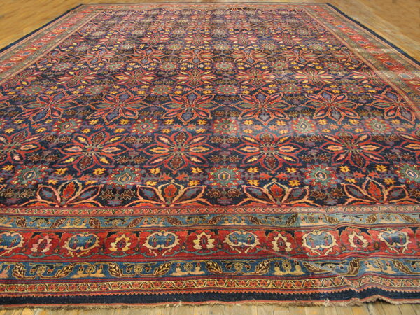 Ornate area rug with repeating red and blue floral patterns and thick, multicolored borders on wood flooring.