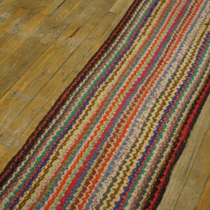 Multicolored braided runner rug with striped design rests on distressed natural wood plank flooring.