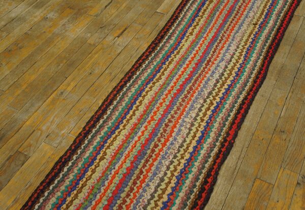 Multicolored braided runner rug with striped design rests on distressed natural wood plank flooring.