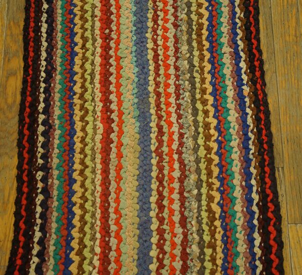 Close-up of a thick, braided runner rug with multicolored vertical stripes on a wood floor.