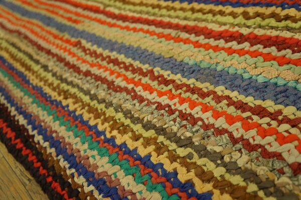 Textured braided rug in multicolor stripes of blue, red, green, tan, and orange on a wood floor.