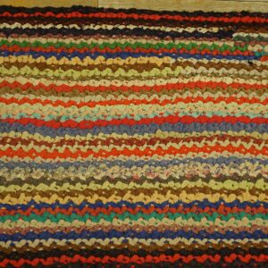 Textured, braided rag rug featuring thick, multihued horizontal stripes on light wood plank flooring.
