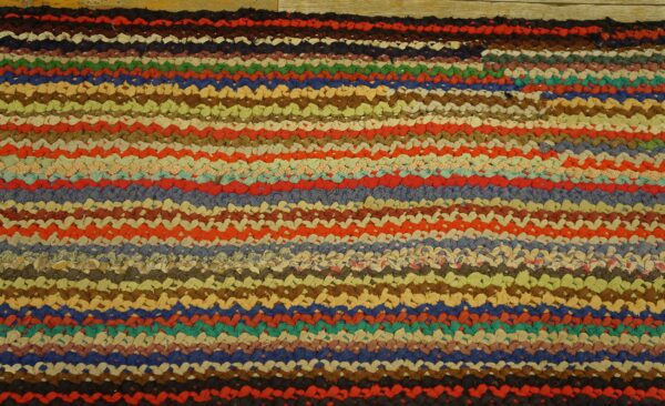 Textured, braided rag rug featuring thick, multihued horizontal stripes on light wood plank flooring.